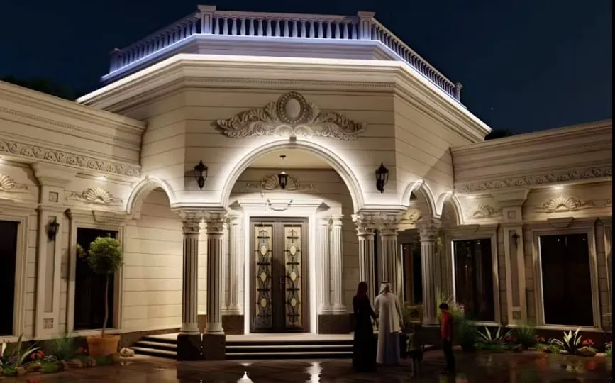 مدخل سكني كلاسيكي مضاء ليلاً بأعمدة ورواق مقوّس